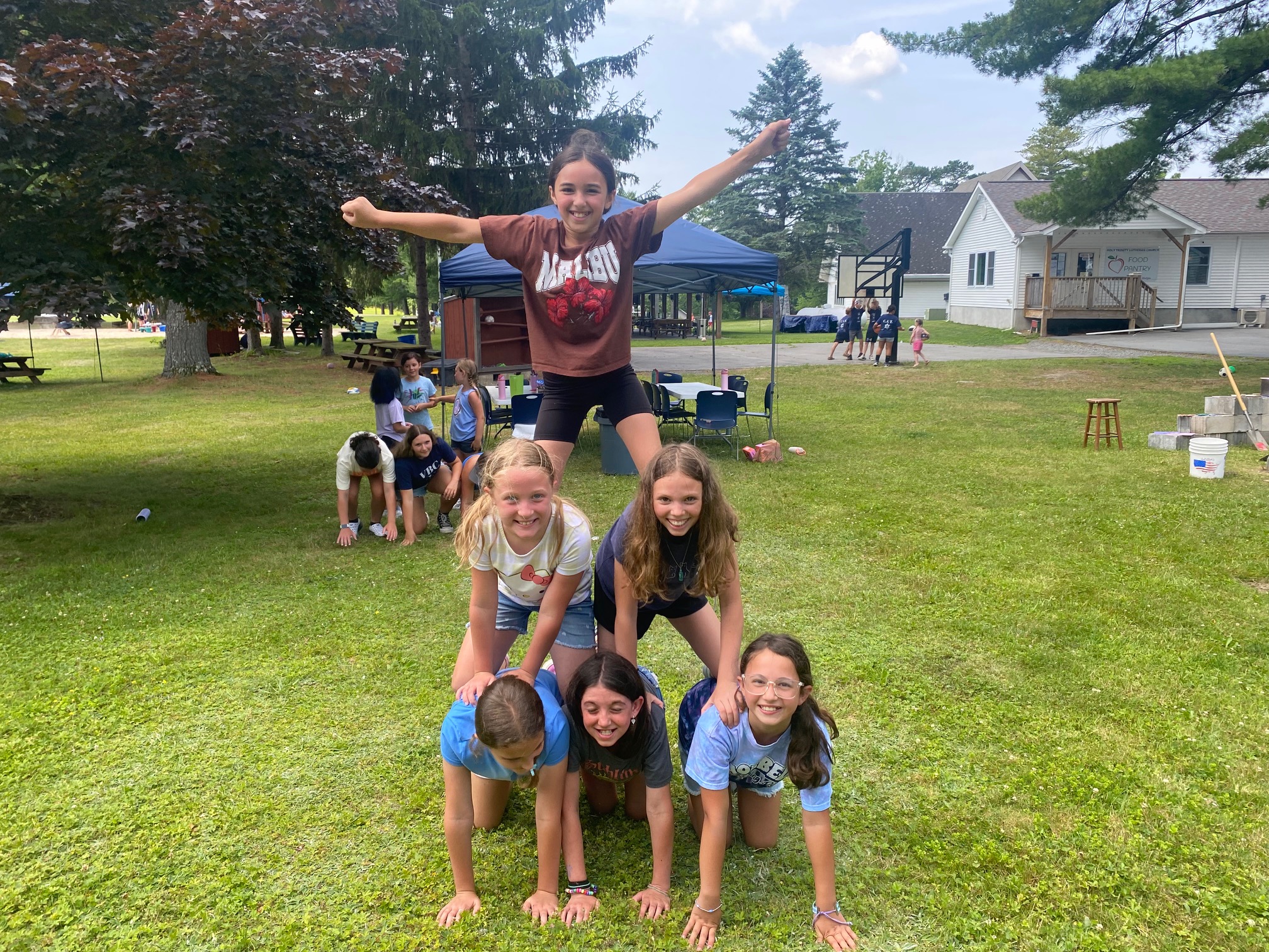 Children smile as they build a human pyramid during an outdoor activity at Holy Trinity's Vacation Bible Camp.